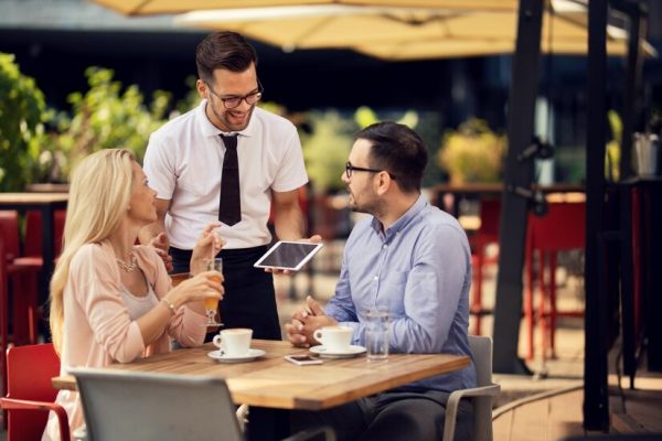 young-happy-waiter-communicating-with-guests-outdoor-cafe_637285-587